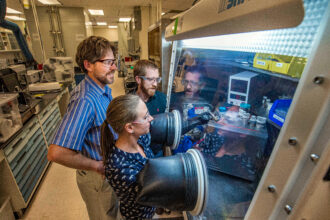 Sandia National Laboratories researchers Leo Small (back right) and Erik Spoerke (back left) observe as Martha Gross (front) works in a glovebox on a new kind of molten-sodium battery. Credit: Randy Montoya