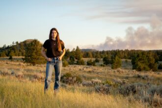 Lead plaintiff Rikki Held on her family's ranch in southeastern Montana. Behind her, a wildfire burns four miles away. In Summer 2022, this was one of 18 wildfires within 50 miles of her home.