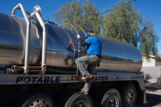 John Hornewer climbs down the ladder of his tanker as he fills it up to haul water from Apache Junction to Rio Verde Foothills, Arizona, on Jan. 7, 2023. Credit: Getty Images